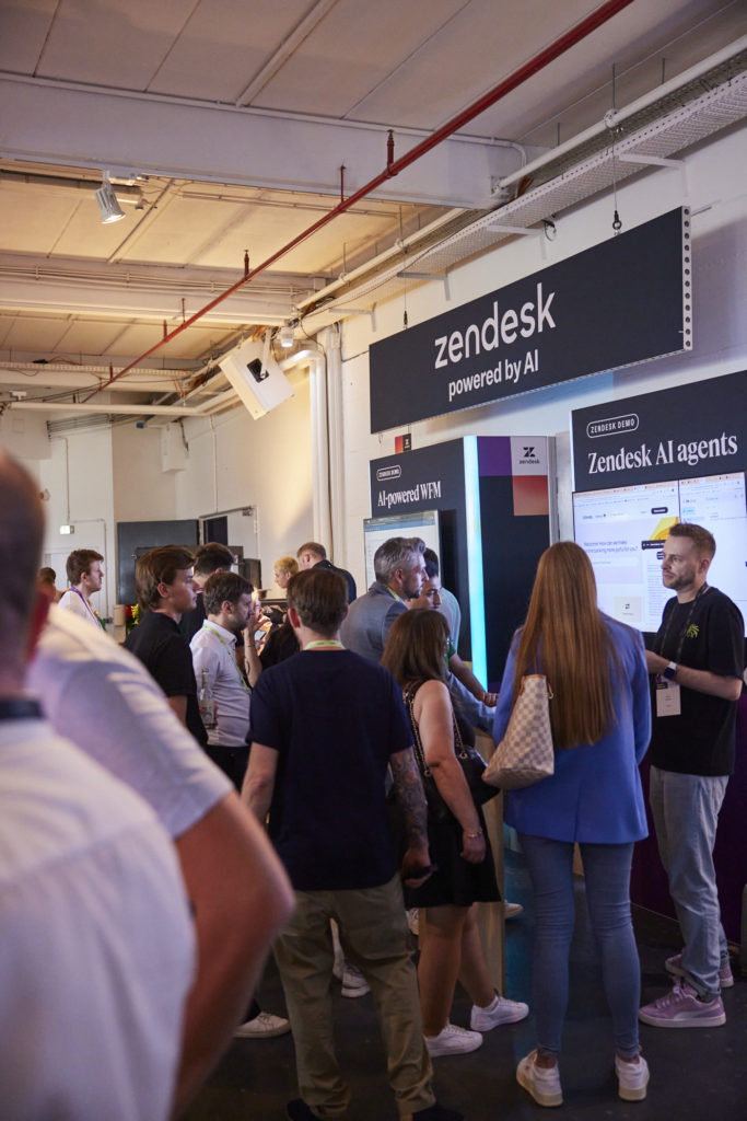 Mehrere Personen stehen vor Demo-Stationen mit den Aufschriften „Zendesk AI agents“ und „AI-powered WFM“.